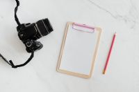 Clipboard and camera on a marble table, copy space