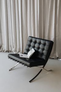 An open book lies on a black leather Barcelona chair