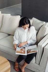 Kaboompics - A young Asian woman sits on the couch and reads a book or magazine
