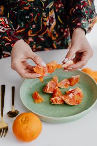 Kaboompics - A woman peels an orange on a green plate