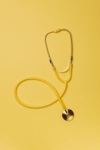 Yellow stethoscope and pills on yellow background