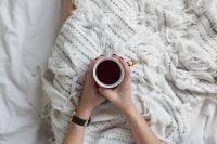 Kaboompics - Soft photo of woman on the bed with the book and cup of tea in hands
