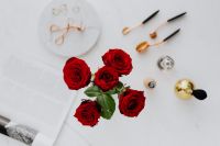 Red roses, gold rings, perfume brushes and make-up accessories on white marble