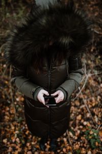Kaboompics - A woman wearing a green winter jacket with a furry hood uses a phone