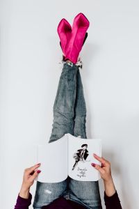 A woman in pink boots and blue jeans reads a book