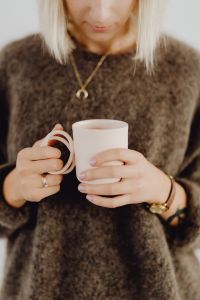 A woman in a brown sweater holds a pink, minimalist mug