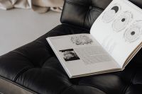 An open book lies on a black leather Barcelona chair