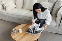Kaboompics - A young Asian woman sits on the couch and reads a book or magazine