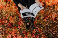Kaboompics - Girl with the Grafconf book on the background of coloured leaves