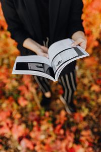 Kaboompics - Girl with the Grafconf book on the background of coloured leaves