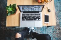 Kaboompics - Woman in ripped jeans and black sneakers with a silver laptop on a wooden table