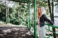 Kaboompics - Blonde woman in a black jacket and ripped jeans by a green handrail