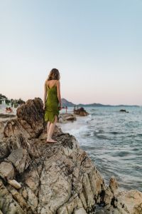 Kaboompics - A woman in a green dress on a rock by the sea
