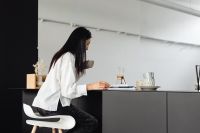 Kaboompics - Adult young Asian woman sits on stool in kitchen - drinks coffee - reads magazine
