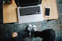 Kaboompics - Woman in ripped jeans and black sneakers with a silver laptop on a wooden table