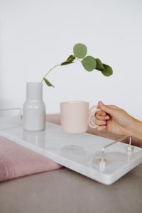 Kaboompics - A woman's hand holds a pink mug or cup over a marble tray