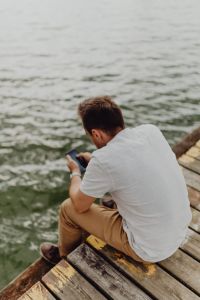 The man is using his phone at the lake