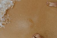 Closeup of sand, feet and small wave