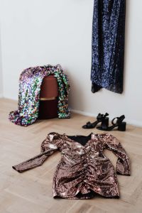 colored sequin dresses and boots lie on a wooden parquet, blue dress hang on the white wall