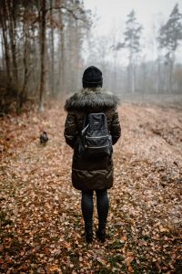 Kaboompics - A woman dressed in a green jacket, a black hat and black trousers with a black backpack in the forest