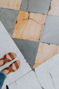 Kaboompics - A woman wearing blue jeans and leather sandals stands on a marble, natural stone floor