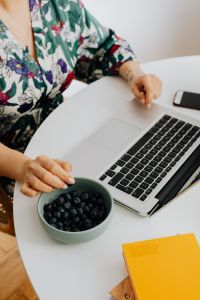 A woman eats blueberries and works on a laptop