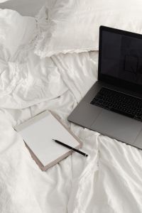 Kaboompics - Working with a laptop in bed - white cotton bedding - blank notebook - pen