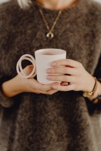 Kaboompics - A woman in a brown sweater holds a pink, minimalist mug