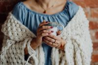 A woman in a warm blanket holds a cup of coffee or tea