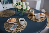 Kaboompics - Round breakfast table with white flowers, golden mats, coffee, croissant and smartphone