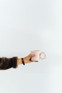 Kaboompics - A woman in a brown sweater holds a pink, minimalist mug