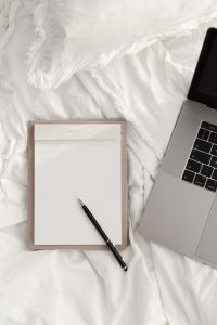 Kaboompics - Working with a laptop in bed - white cotton bedding - blank notebook - pen