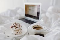 Macbook, a coffee, a chocolate, a meringue dessert and a notebook in a bed