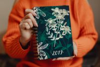 A woman in an orange sweater holds the 2019 calendar in her hands