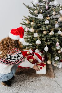 Kaboompics - Woman with Gift Wearing Christmas Sweater and Santa Hat, Christmas Tree Background