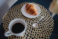 Kaboompics - Coffee cup with a croissant on a golden mat