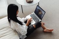 Adult young Asian woman sits in living room and works on laptop