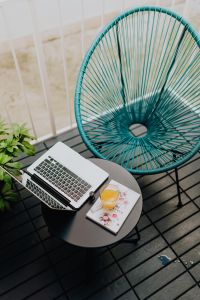 Kaboompics - A stylish garden chair and a small table on the balcony. Macbook laptop, book and a glass of orange juice.