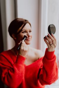 A woman in a red sweater does her make-up - applies a foundation with a brush