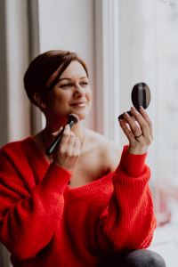 Kaboompics - A woman in a red sweater does her make-up - applies a foundation with a brush