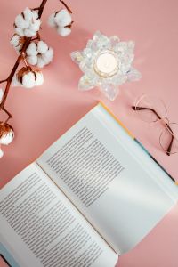 Kaboompics - An open book, candle, glasses and a cotton branch on a pink background