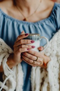 Kaboompics - A woman in a warm blanket holds a cup of coffee or tea