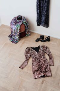colored sequin dresses and boots lie on a wooden parquet, blue dress hang on the white wall