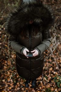 Kaboompics - A woman wearing a green winter jacket with a furry hood uses a phone