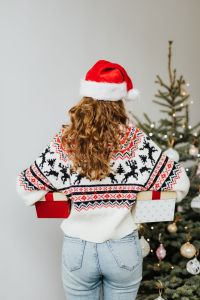 Kaboompics - Woman with Gift Wearing Christmas Sweater and Santa Hat, Christmas Tree Background
