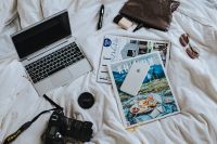 Kaboompics - Silver laptop, a camera, magazines and an iphone on white bed sheets