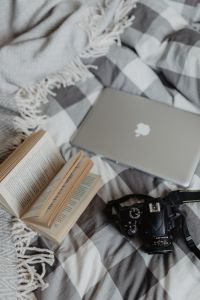 A camera, MacBook, and a book waiting in bed